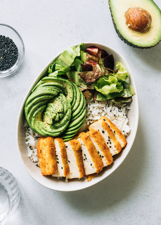 healthy rice bowl topped with avocado, tofu and lettuce