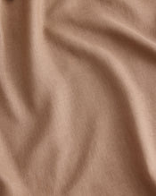 A close-up of draped fabric in a warm taupe-beige colour called Portobello, in 100% French flax linen showing soft folds and a fine woven texture. - view