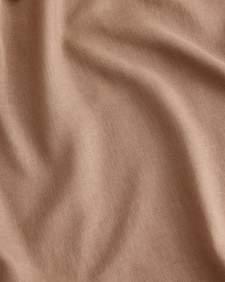 A close-up of draped fabric in a warm taupe-beige colour called Portobello, in 100% French flax linen showing soft folds and a fine woven texture.