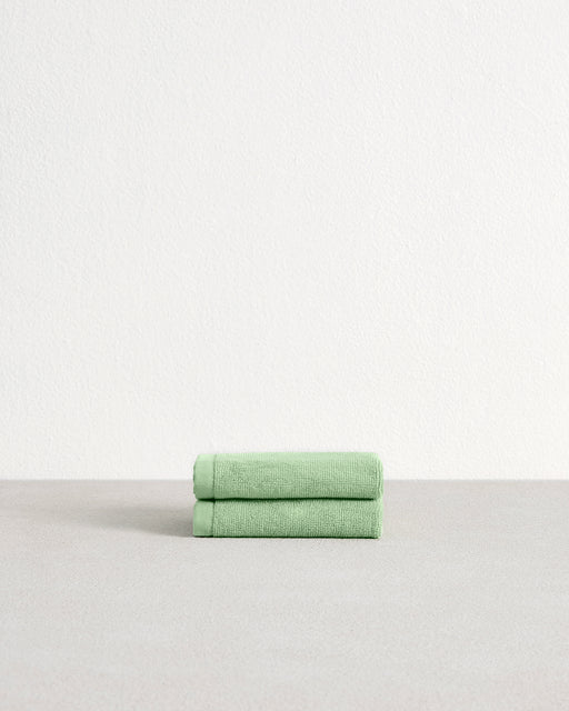 A set of two Apple 100% Cotton Terry Face Washers by Bed Threads, crafted from absorbent, skin-friendly cotton, is neatly folded on a light gray surface with a plain white wall in the background.