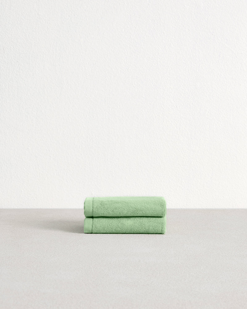 A set of two Apple 100% Cotton Terry Face Washers by Bed Threads, crafted from absorbent, skin-friendly cotton, is neatly folded on a light gray surface with a plain white wall in the background.
