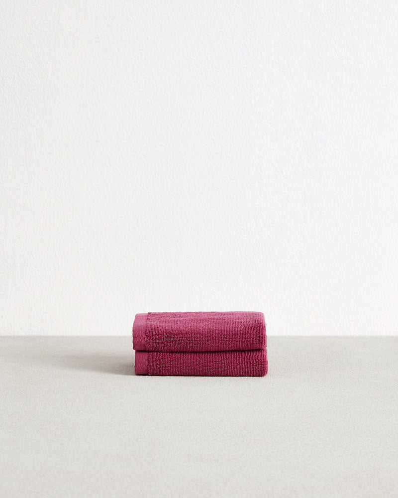 A set of two Berry 100% Cotton Terry Face Washers by Bed Threads, neatly folded in dark pink, is displayed on a light grey surface with a plain white background.