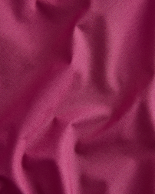 A close-up of the Berry 100% Organic Cotton Flat Sheet by Bed Threads, featuring soft magenta percale with gentle folds and GOTS certified breathable fabric.