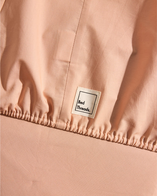 A close-up of a Bed Threads Butterscotch 100% Organic Cotton Fitted Sheet Set with an elastic edge and white label, showcasing GOTS certified bedding.