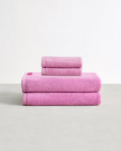 Set of two bubblegum pink face washers and two hand towels in 100% cotton terry stacked on a light grey surface with a white background.  - view