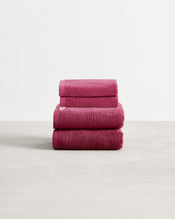 A stack of two, organic cotton terry hand towels and two face washers in a berry pink shade. - view