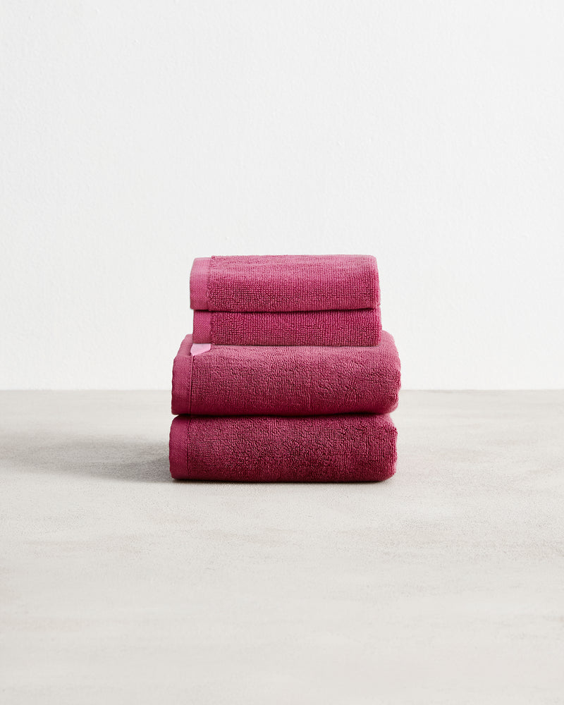 A stack of two, organic cotton terry hand towels and two face washers in a berry pink shade.