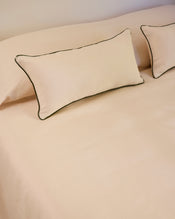 Two Crème & Olive 100% French Flax Linen Piped Lumbar Cushion Covers by Bed Threads rest on a matching beige bedspread, creating a simple and neatly arranged bedding setup. - view
