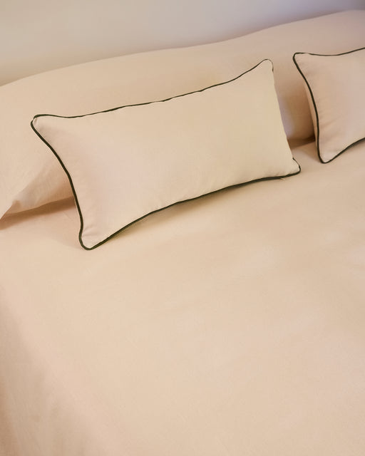 Two Crème & Olive 100% French Flax Linen Piped Lumbar Cushion Covers by Bed Threads rest on a matching beige bedspread, creating a simple and neatly arranged bedding setup.