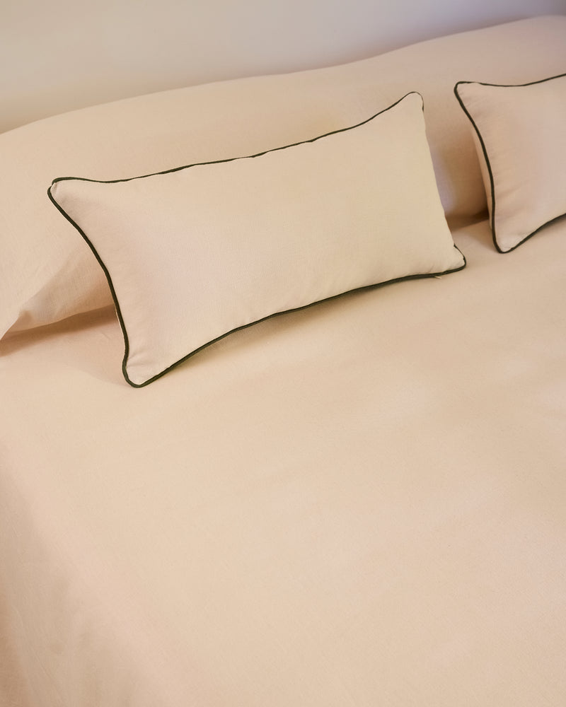 Two Crème & Olive 100% French Flax Linen Piped Lumbar Cushion Covers by Bed Threads rest on a matching beige bedspread, creating a simple and neatly arranged bedding setup.