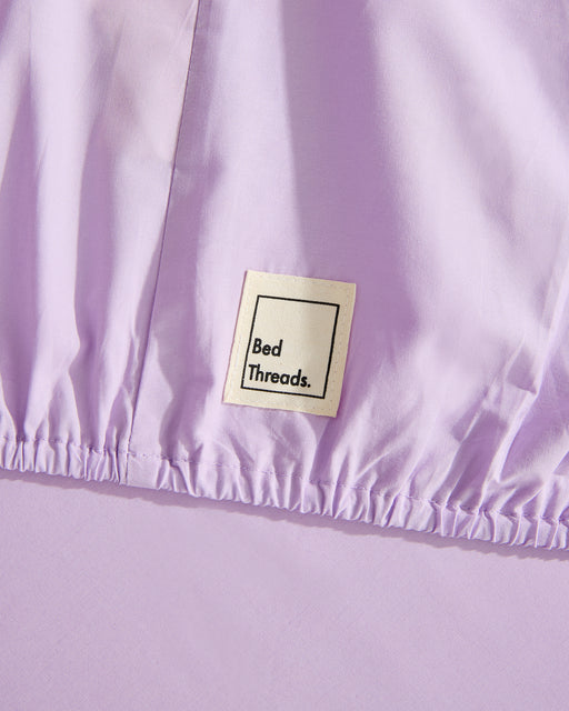 The Violet 100% Organic Cotton Fitted Sheet by Bed Threads features a stitched black Bed Threads label near the elastic edge—a stylish and natural addition to your bedding collection.