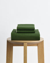 Two green hardcover books rest on a light wooden stool against a white background, echoing the soothing hues of the Bed Threads Moss, Apple & Vanilla Piped 100% Organic Cotton Duvet Cover Set. - view