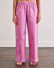 A person stands barefoot on a wooden floor, wearing Bed Threads Bubblegum & Berry Piped Pants—relaxed, breathable cotton with an elasticated waist. The cropped photo shows them from shoulders down against a plain white wall. - view
