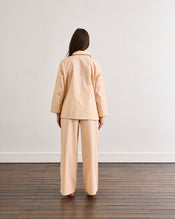 A person with long hair stands barefoot on a wooden floor, facing a plain white wall, wearing the Bed Threads Vanilla & Espresso Piped Long Sleeve Shirt. - view