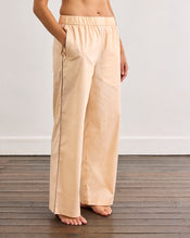 A person stands barefoot on a wooden floor, wearing Bed Threads' Vanilla & Espresso Piped Pants—relaxed, breathable cotton pants with a comfy elastic waist and pockets. The upper body is not visible. - view
