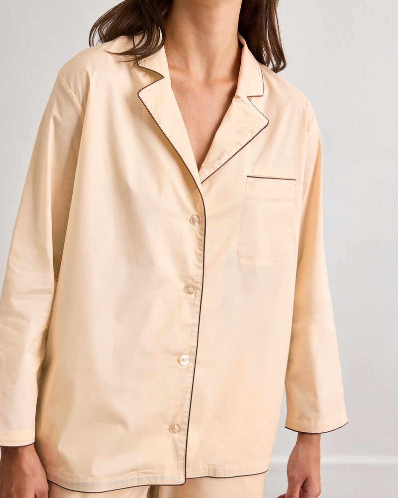 A person wears the Bed Threads Vanilla & Espresso Piped Long Sleeve Shirt, a light beige cotton set with contrast piping, chest pocket, and long sleeves. The image is cropped at the neck and knees.