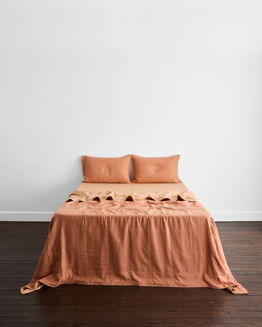 A minimalistic room features a neatly made bed with the Bed Threads Terracotta & Hazelnut 100% French Flax Linen Quilt Set against a plain white wall and dark wood floor.