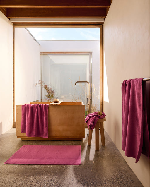 A close-up of the Berry Cotton Terry Bath Sheet by Bed Threads shows its pink textured surface and folded hanging loop, highlighting the plush softness of this cotton bath sheet—ideal for adding luxury comfort to your bathroom.