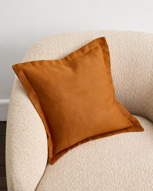 An Oatmeal 100% French Flax Linen Cushion Cover by Bed Threads is arranged neatly on a wooden stool, set against a plain white wall.