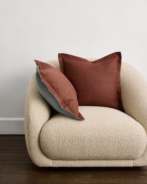 An Oatmeal 100% French Flax Linen Cushion Cover by Bed Threads is arranged neatly on a wooden stool, set against a plain white wall.