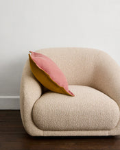 A modern cream armchair sits on a dark wooden floor, topped with a Bed Threads Pink Clay & Turmeric 100% French Flax Linen Cushion Cover. A plain white wall forms the background. - view