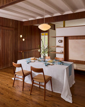 A dining room with wood-paneled walls and floor features a Bed Threads White & Lagoon 100% French Flax Linen Table Bundle on the table, set for a meal with dishes and glassware. Two wooden chairs are placed at the table. - view
