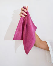 A hand holds a neatly folded, bright pink Berry 100% Cotton Terry Face Washer from Bed Threads (set of two) against a plain white background. - view
