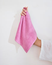 A hand with light pink nail polish holds a Bubblegum 100% Cotton Terry Face Washer by Bed Threads, made from soft, absorbent terry that's gentle on skin, shown against a plain white background. Set includes two washers. - view
