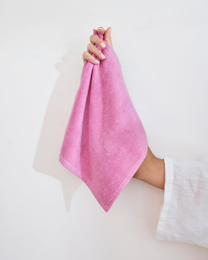 A hand with light pink nail polish holds a Bubblegum 100% Cotton Terry Face Washer by Bed Threads, made from soft, absorbent terry that's gentle on skin, shown against a plain white background. Set includes two washers.