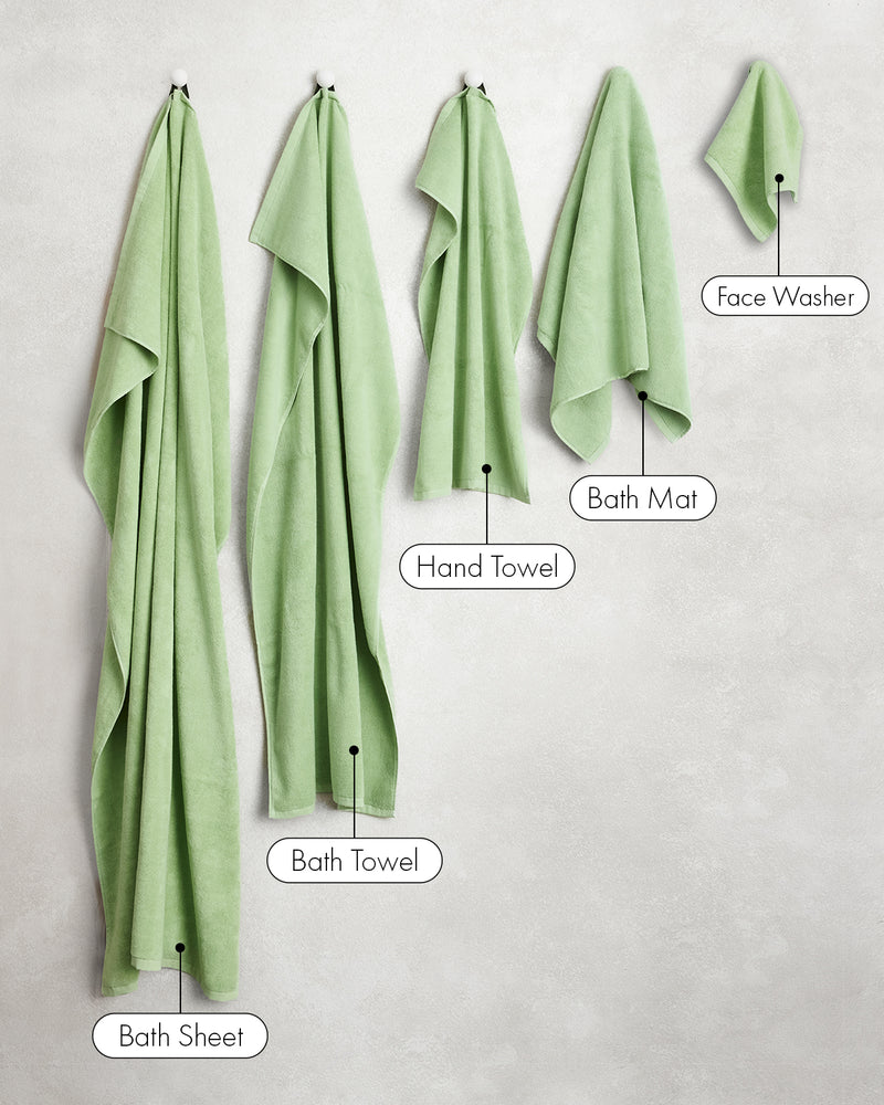 Five green towels from the Bed Threads Apple 100% Cotton Terry Bath Towel Bundle hang on hooks, labeled left to right: Bath Sheet, Bath Towel, Hand Towel, Bath Mat, and Face Washer.