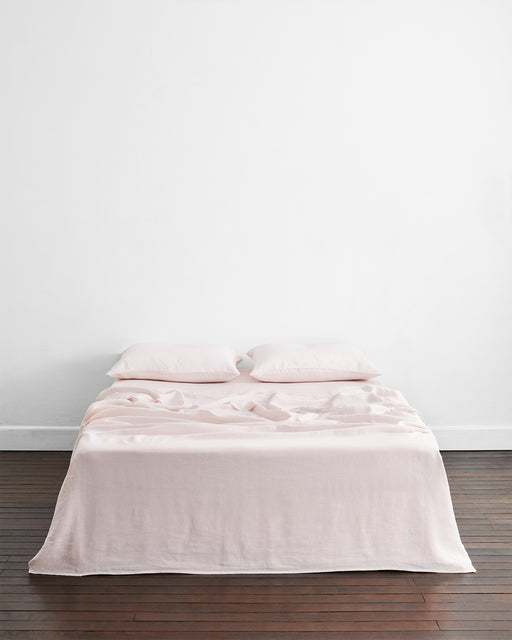 A neatly made bed features two Bed Threads Rosewater 100% French Flax Linen King Pillowcases against a plain white wall, set on a dark wooden floor.