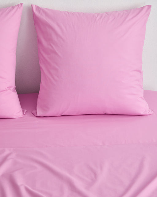 Two large, square pillows with Bubblegum 100% Organic Cotton European Pillowcases by Bed Threads are neatly arranged on a bed with matching pink sheets against a light wall, creating a smooth and coordinated look.