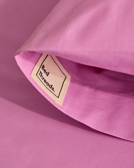 A close-up of a folded pink bedsheet with a beige Bed Threads label highlights its soft texture, pairing perfectly with Bed Threads' Bubblegum Organic Cotton Pillowcases (Set of Two).