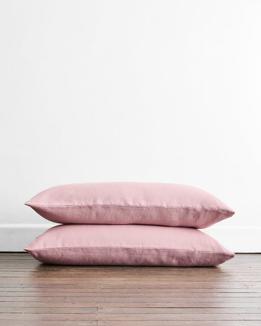 Two Lavender 100% French Flax Linen King Pillowcases by Bed Threads are stacked together on a wooden floor against a plain white wall.