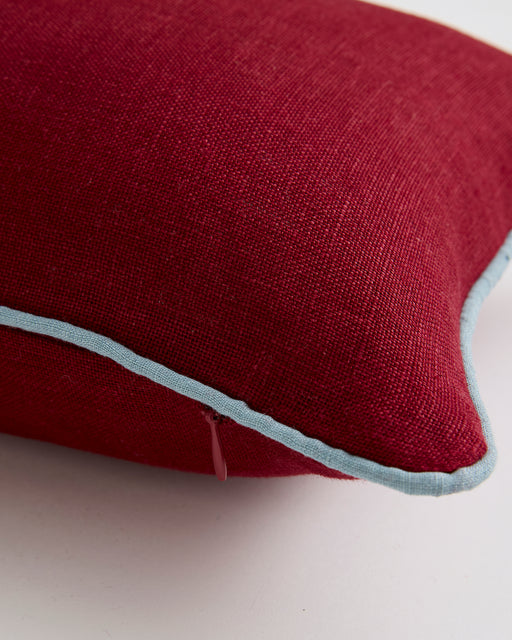 A close-up of the Bed Threads Mulberry & Lagoon 100% French Flax Linen Piped Lumbar Cushion Cover, featuring red linen with light blue piping and a small side zipper, set against a plain white background.