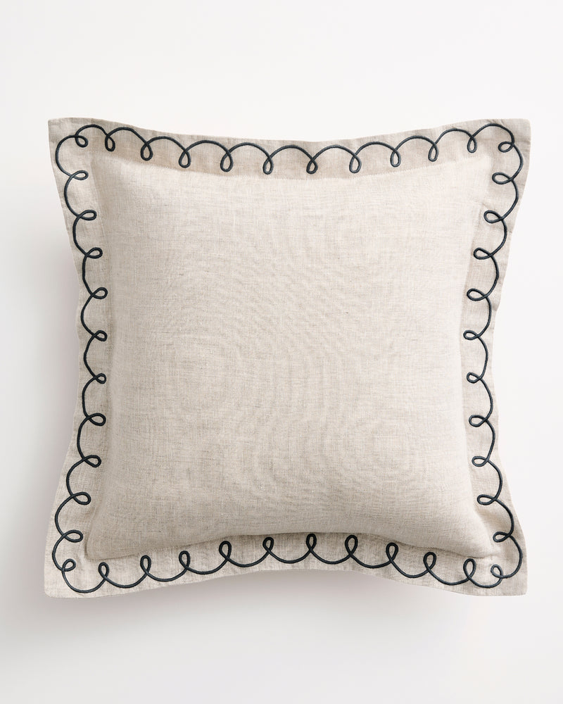 The Bed Threads Oatmeal & Charcoal 100% French Flax Linen Swirl Cushion Cover features a square design with a black embroidered swirl edge, crafted from textured linen for a modern minimalist look, shown on a white background.