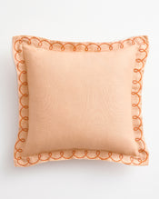 The Bed Threads Terracotta & Pink Clay 100% French Flax Linen Swirl Cushion Cover features a peach hue with a sheer border and orange swirl edge embroidery, shown on a white background. - view
