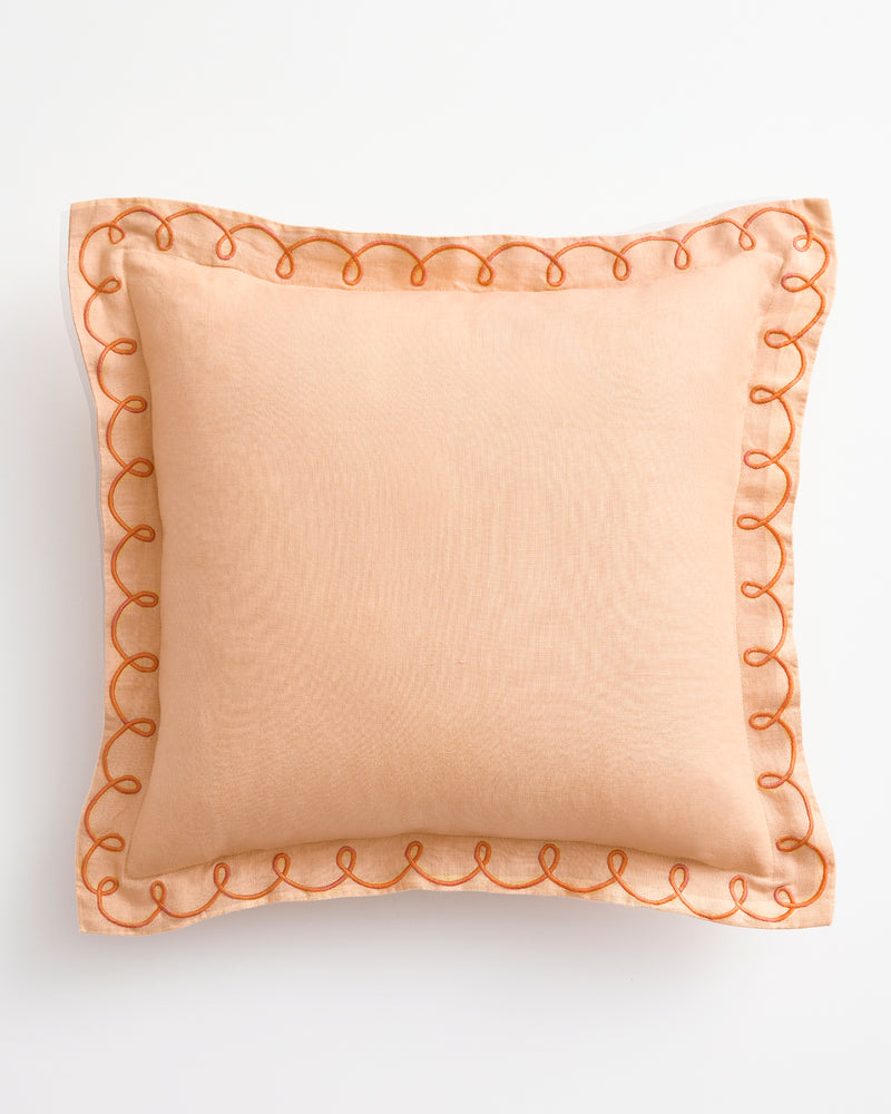 The Bed Threads Terracotta & Pink Clay 100% French Flax Linen Swirl Cushion Cover features a peach hue with a sheer border and orange swirl edge embroidery, shown on a white background.