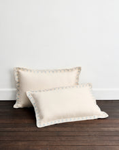 Two Crème & Coast 100% French Flax Linen Swirl Pillowcases by Bed Threads rest against a white wall on a dark wooden floor, featuring elegant embroidered edges and offering the perfect upgrade for breathable linen bedding. - view