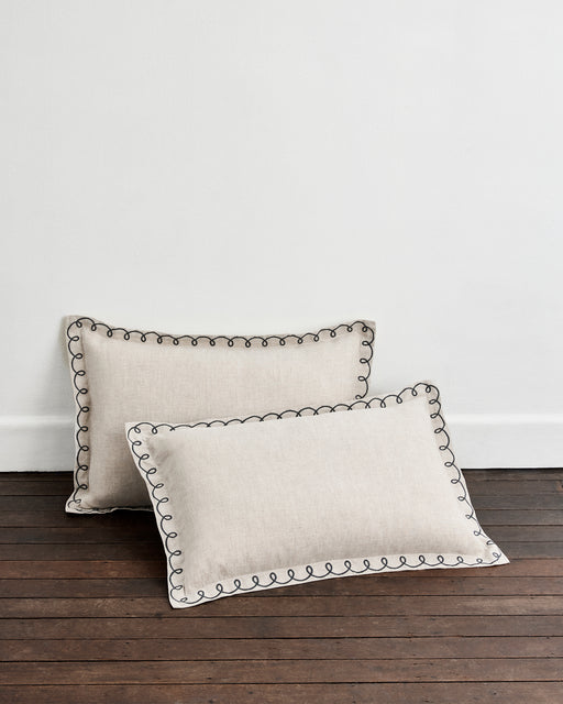 A pair of Bed Threads Oatmeal & Charcoal 100% French Flax Linen Swirl Pillowcases rests on a dark wooden floor against a plain white wall.