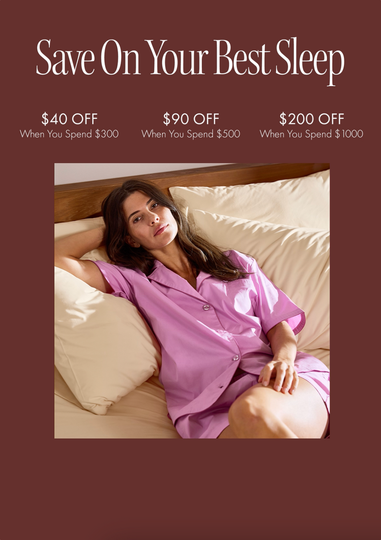 Woman in lavender pajamas lounging on a bed with beige sheets; text above offers $40 off $300, $90 off $500, and $200 off $1000 purchases on a maroon background.