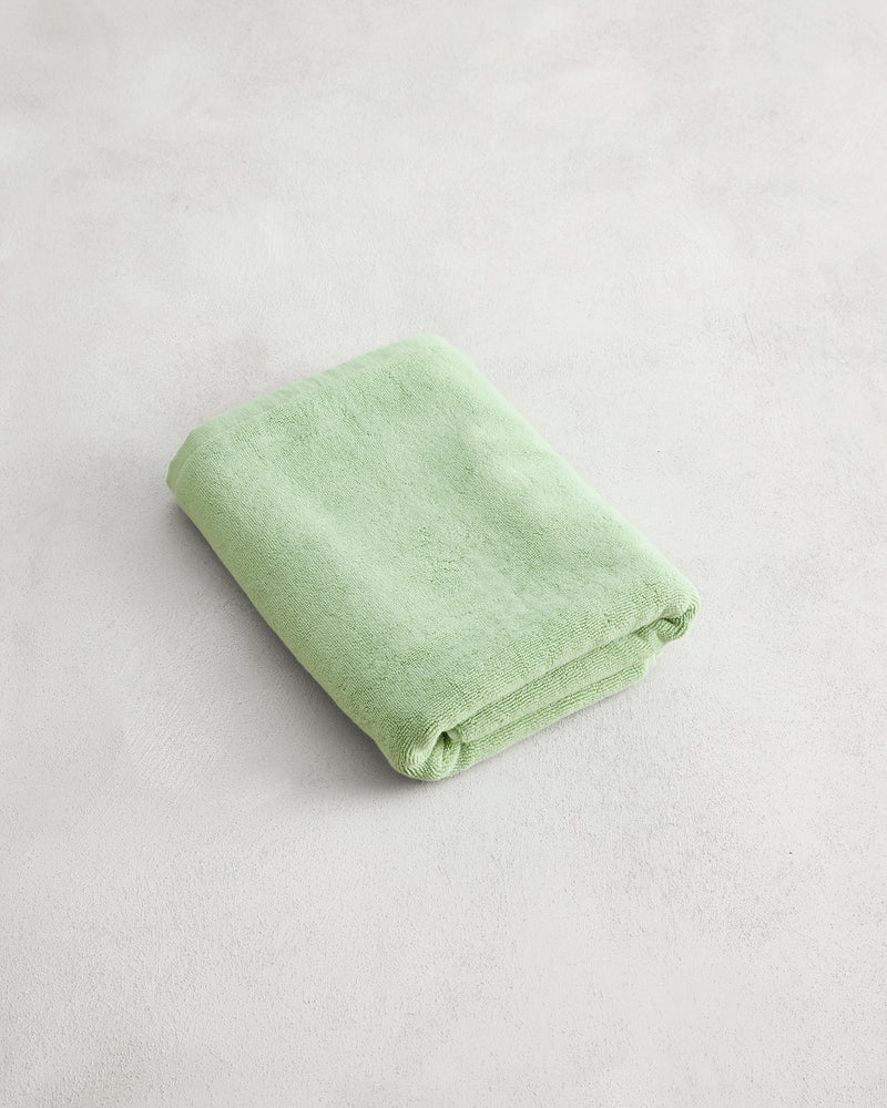 A neatly folded Apple 100% Cotton Terry Bath Mat by Bed Threads in light green rests on a plain, light-colored surface.