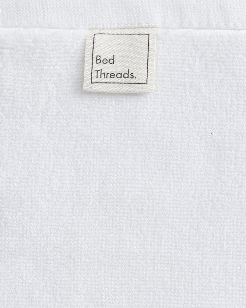 A close-up of Crisp White 100% Cotton Terry Face Washers (Set of Two) from Bed Threads, featuring a beige label and soft, absorbent terry that’s gentle on skin for everyday comfort.
