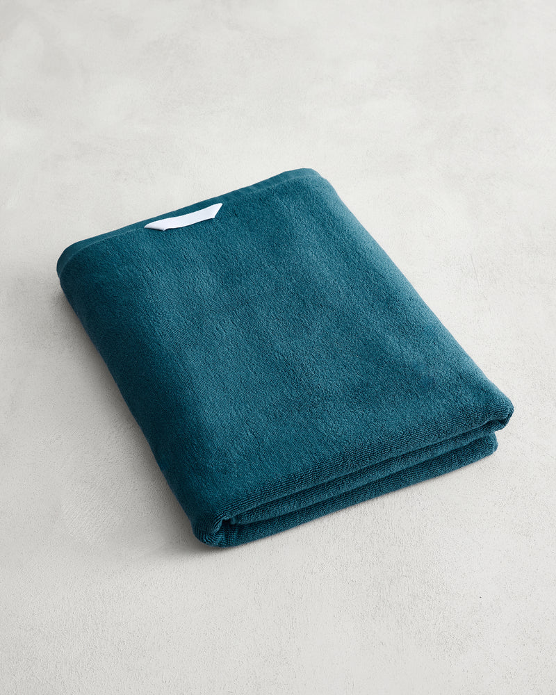 Aegean 100% Cotton Terry Bath Sheet by Bed Threads in plush teal, neatly folded with a small white label, sits on a light gray textured surface—ideal for those seeking quick-drying cotton bath sheets.