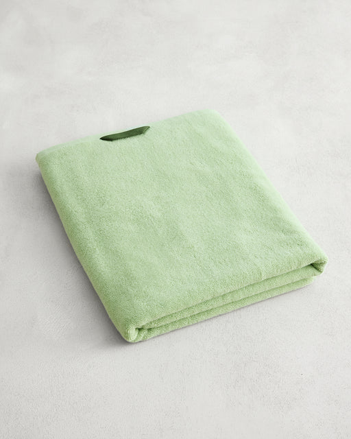 The Bed Threads Apple 100% Cotton Terry Bath Sheet, neatly folded in light green, rests on a light gray textured surface, bringing a touch of luxury to your space.