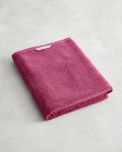 The Bed Threads Berry 100% Cotton Terry Bath Sheet, in plush raspberry, is neatly folded on a light gray surface with a light pink hanging loop visible. Quick-drying and stylishly functional, it's the perfect towel for any bathroom. - view