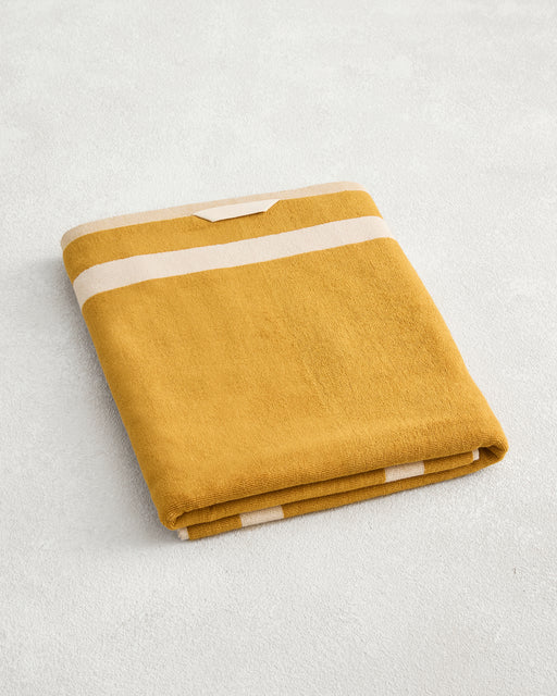 The Bed Threads Crème & Turmeric Two-Toned 100% Cotton Terry Bath Sheet, plush and quick-drying, is folded neatly on a light surface, showcasing its soft yellow and white striped design.