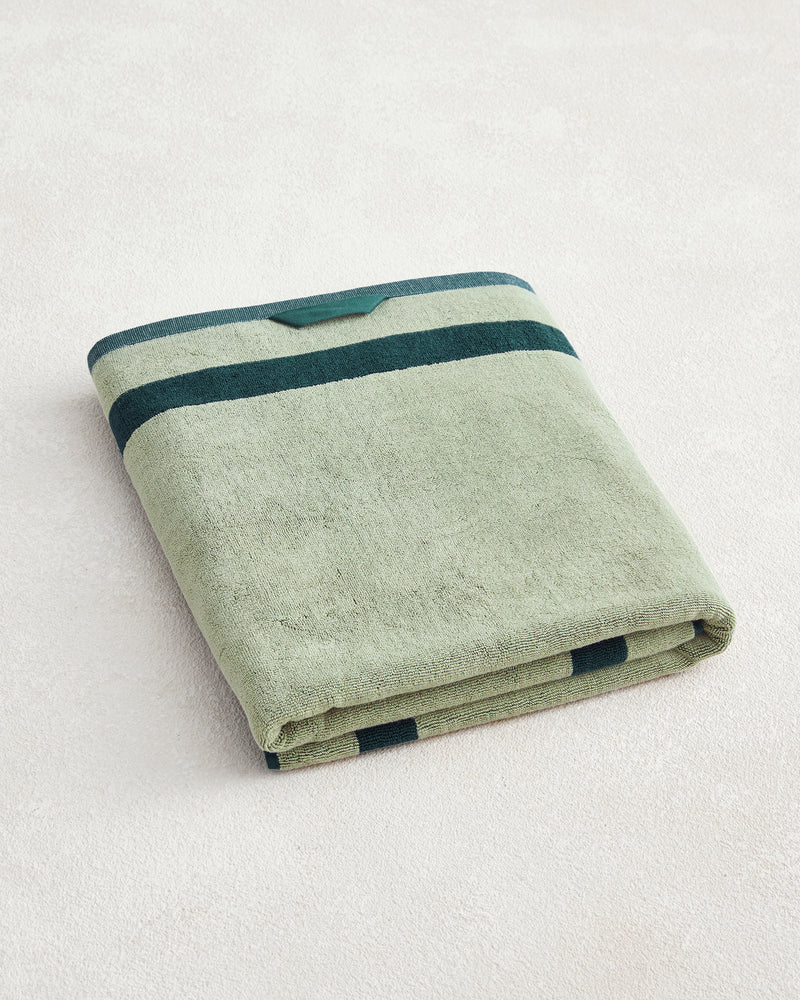 The Bed Threads Forest & Sage Two-Toned 100% Cotton Terry Bath Sheet features a folded light green design with two dark green stripes near the edges, crafted from soft cotton and displayed on a light textured surface.