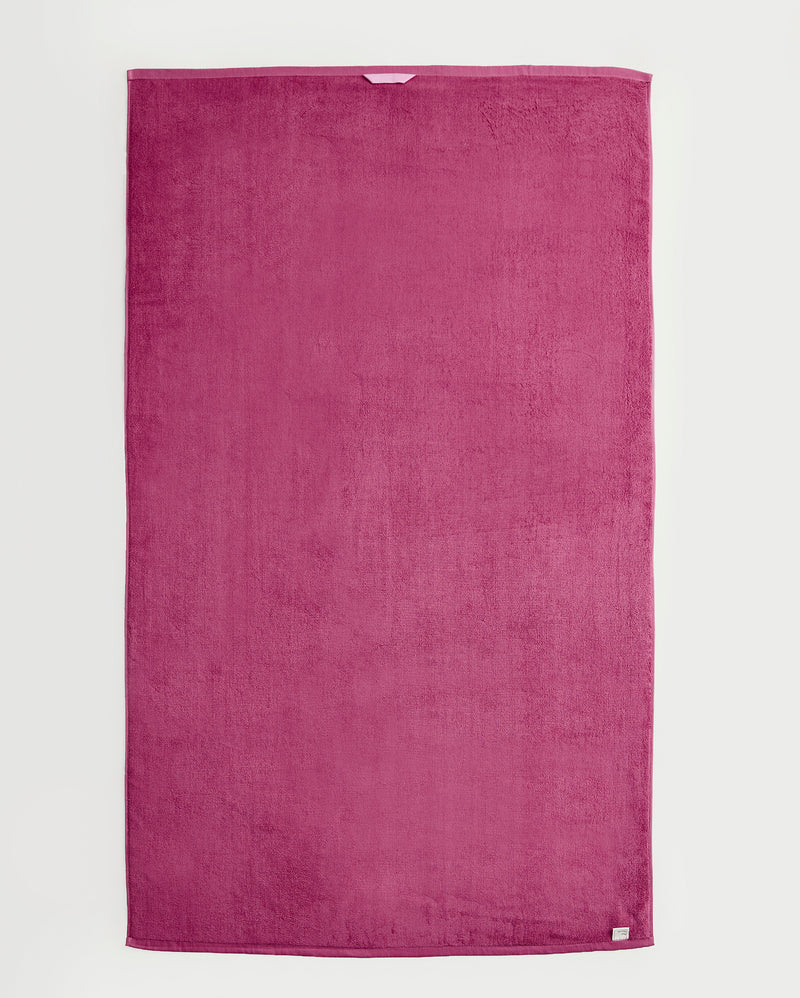 A large, rectangular magenta Berry 100% Cotton Terry Bath Sheet by Bed Threads is laid flat on a white background. The plush towel has a soft texture and features a small white label on one corner.