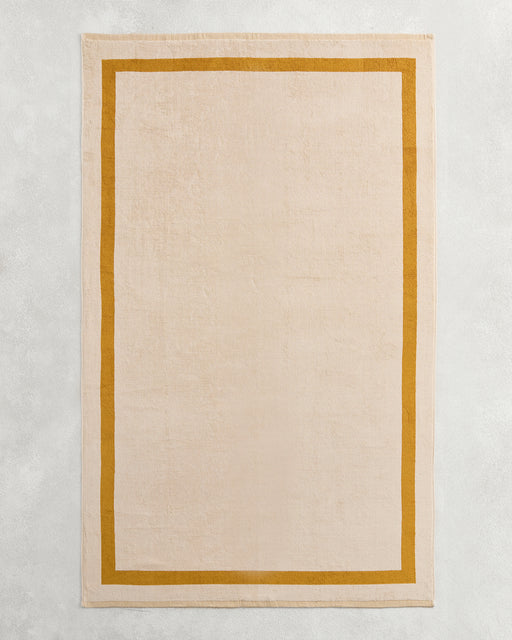 The Bed Threads Crème & Turmeric Two-Toned 100% Cotton Terry Bath Sheet adds cozy style to your bathroom, especially when paired with a rectangular beige rug on a light grey textured surface for an inviting touch.
